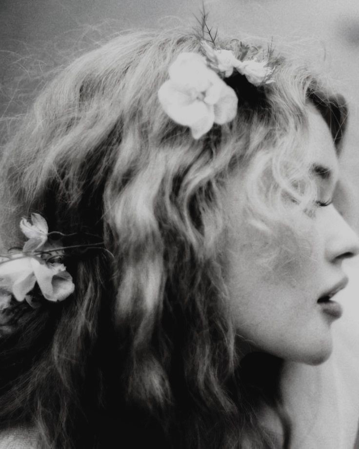A woman in profile with white flowers in her hair, in black and white