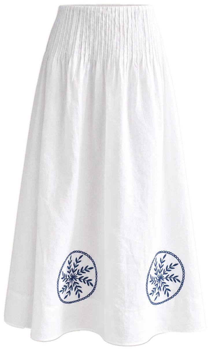 The Josefina Skirt, white linen with a smocked waist and two blue embroidered medallions at the hem, shown as if worn
